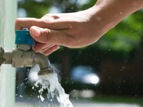 A hand turning an outdoor shutoff valve with water flowing