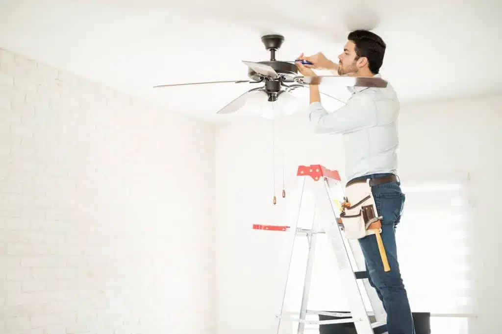 Tech installing a ceiling fan from a step ladder